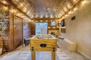 Una habitación con suelo de madera, una mesa de fútbol de mesa, una ventana y una puerta.