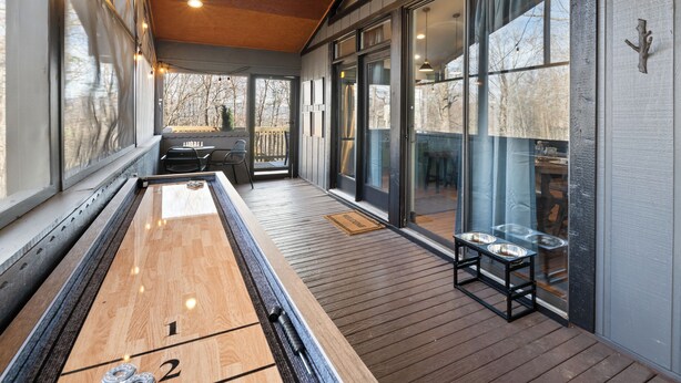 Une table de jeu de «shuffleboard» sur une terrasse en bois, avec vue sur une chaise longue et une porte vitrée donnant sur l’extérieur.
