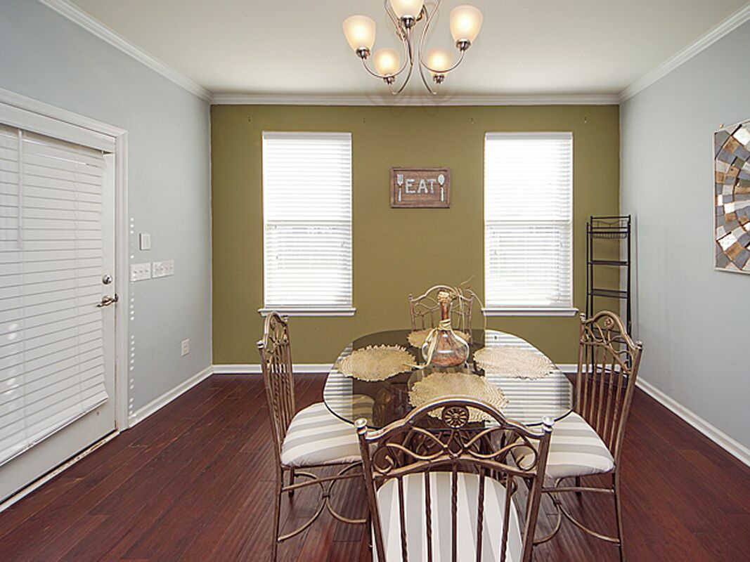 A dining room with a glass table, four chairs, a chandelier, and a 'EAT' sign on the wall.
