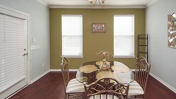 A dining room with a glass table, four chairs, a chandelier, and a 'EAT' sign on the wall.