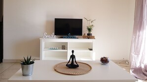 Un suport de televisió blanc amb un televisor de pantalla plana, una petita planta en test i elements decoratius, incloent un cartell amb lletres i una petita estàtua.