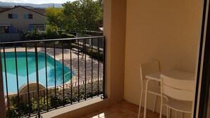 Un balcó amb vistes a una piscina, una taula blanca i una cadira.
