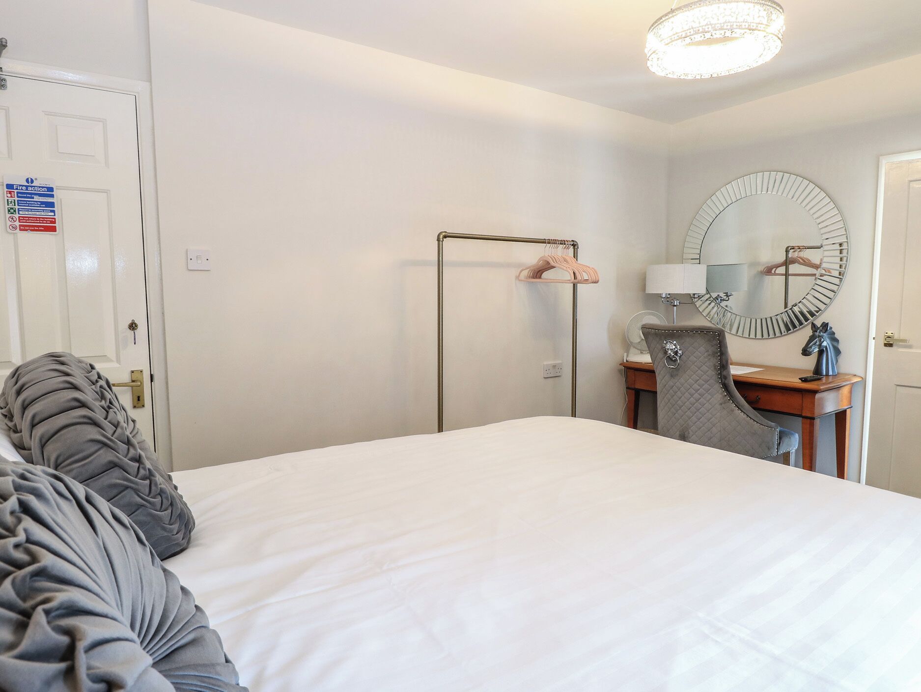 A hotel room with a bed, a desk, a chair, a mirror, and a hanging towel rack.