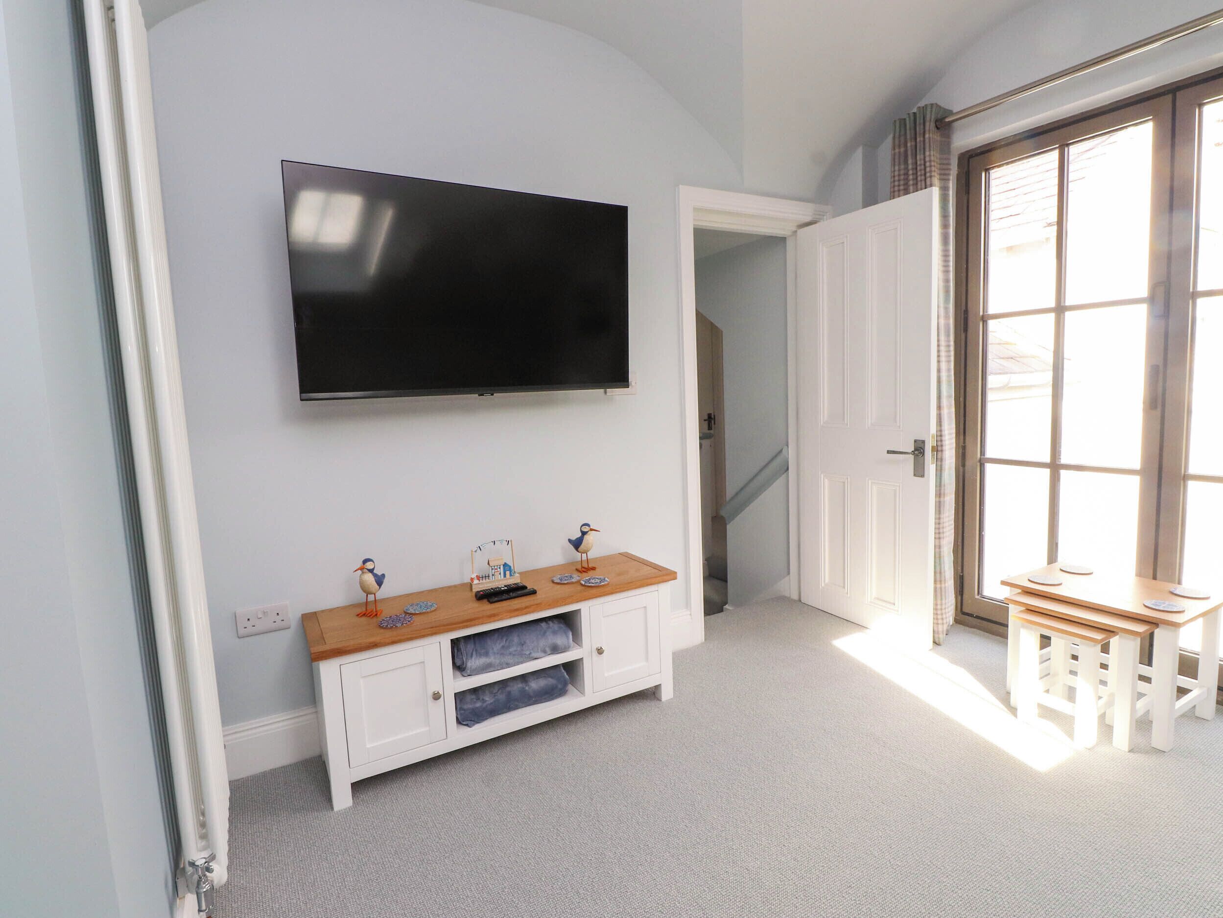 Una habitación con una televisión montada en la pared, un armario blanco con tapa de madera y una puerta que da a otra habitación.