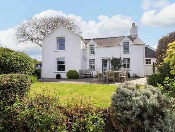 A two-story white house with a well-maintained lawn, a bench, and a table with chairs in the front yard. - Bryn Tirion (Pwllheli)