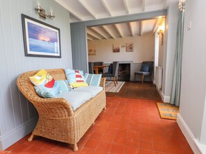 A wicker sofa with colorful cushions, a fireplace, and a dining area with chairs.