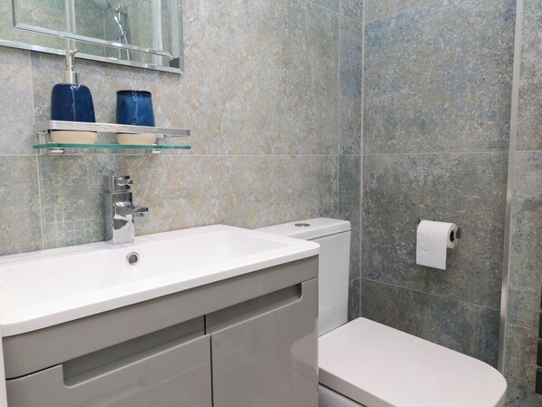 A bathroom with a white sink, a toilet, and a glass shelf above the sink.