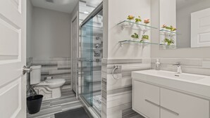 Een moderne badkamer met een douchecabine van glas, een witte wastafel en een spiegel met een glazen plank waarop planten staan.