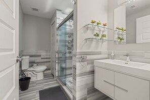 Een moderne badkamer met een douchecabine van glas, een witte wastafel en een spiegel met een glazen plank waarop planten staan.