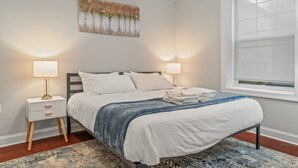 Een slaapkamer met een bed, twee nachtkastjes, een raam en een kunstwerk aan de muur.