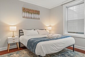 Een slaapkamer met een bed, twee nachtkastjes, een raam en een kunstwerk aan de muur.