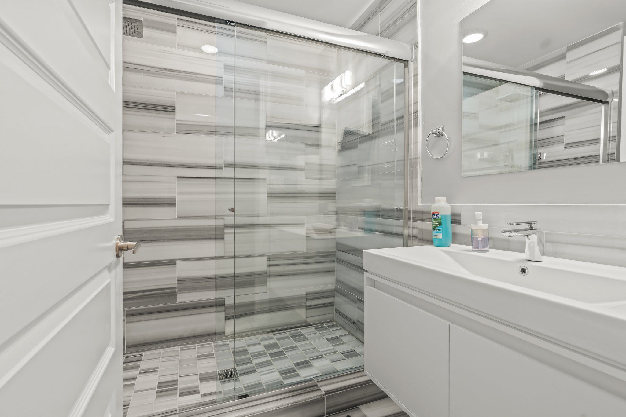 A modern bathroom with a glass shower enclosure, a white vanity, and a mirror above the sink.
