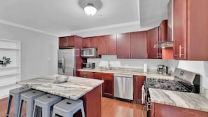 A modern kitchen with a marble countertop, stainless steel appliances, and wooden cabinets.