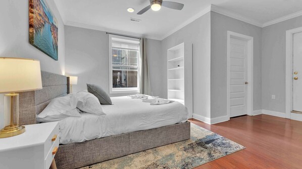 A bedroom with a bed, bedside table, lamp, window, and a view of the city.