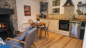 A cozy living room with a fireplace, a dining area with a wooden table and chairs, and a kitchen with modern appliances and a brick backsplash.