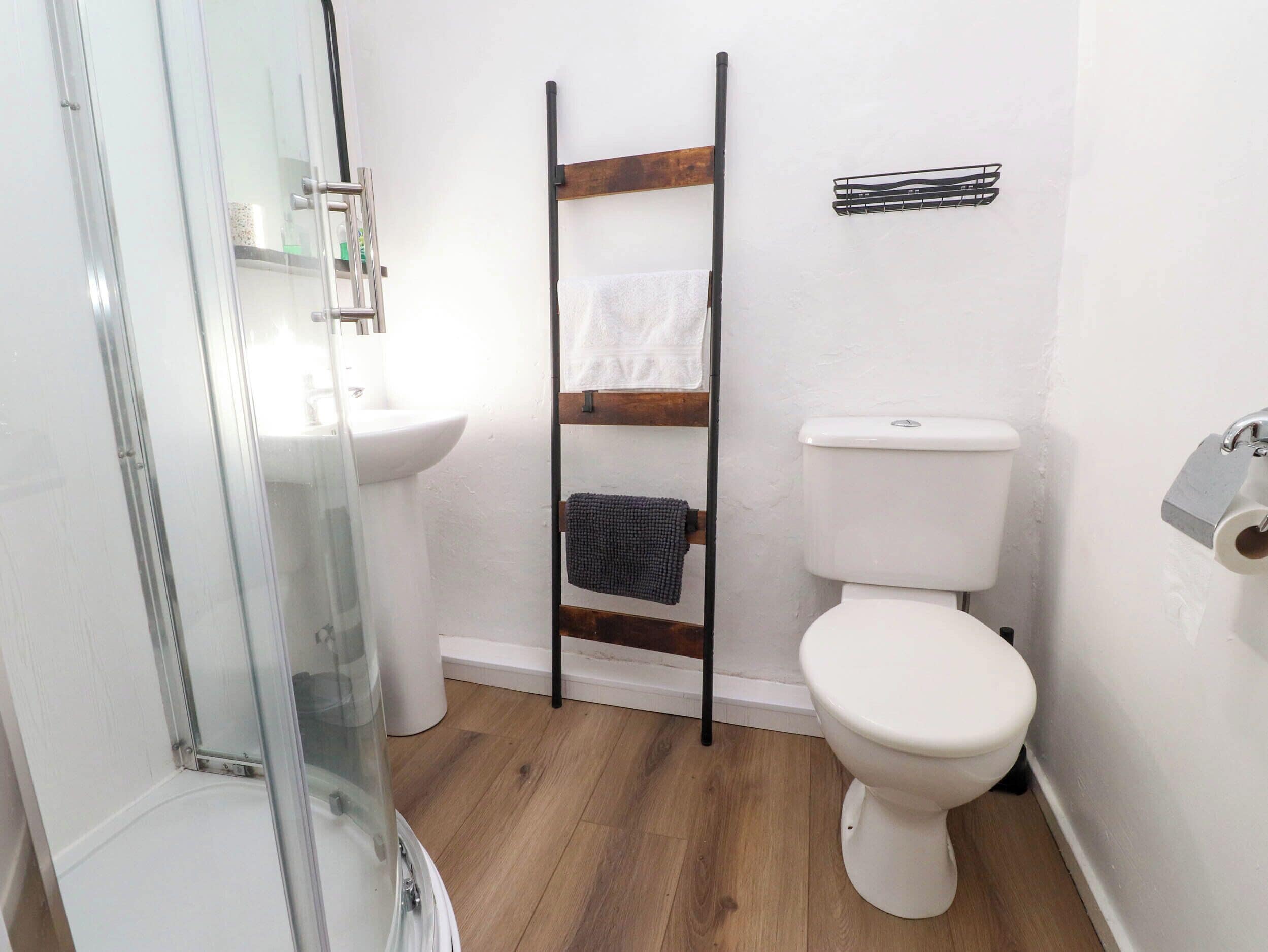 A bathroom with a glass shower enclosure, a white sink, a wooden towel rack, and a white toilet.