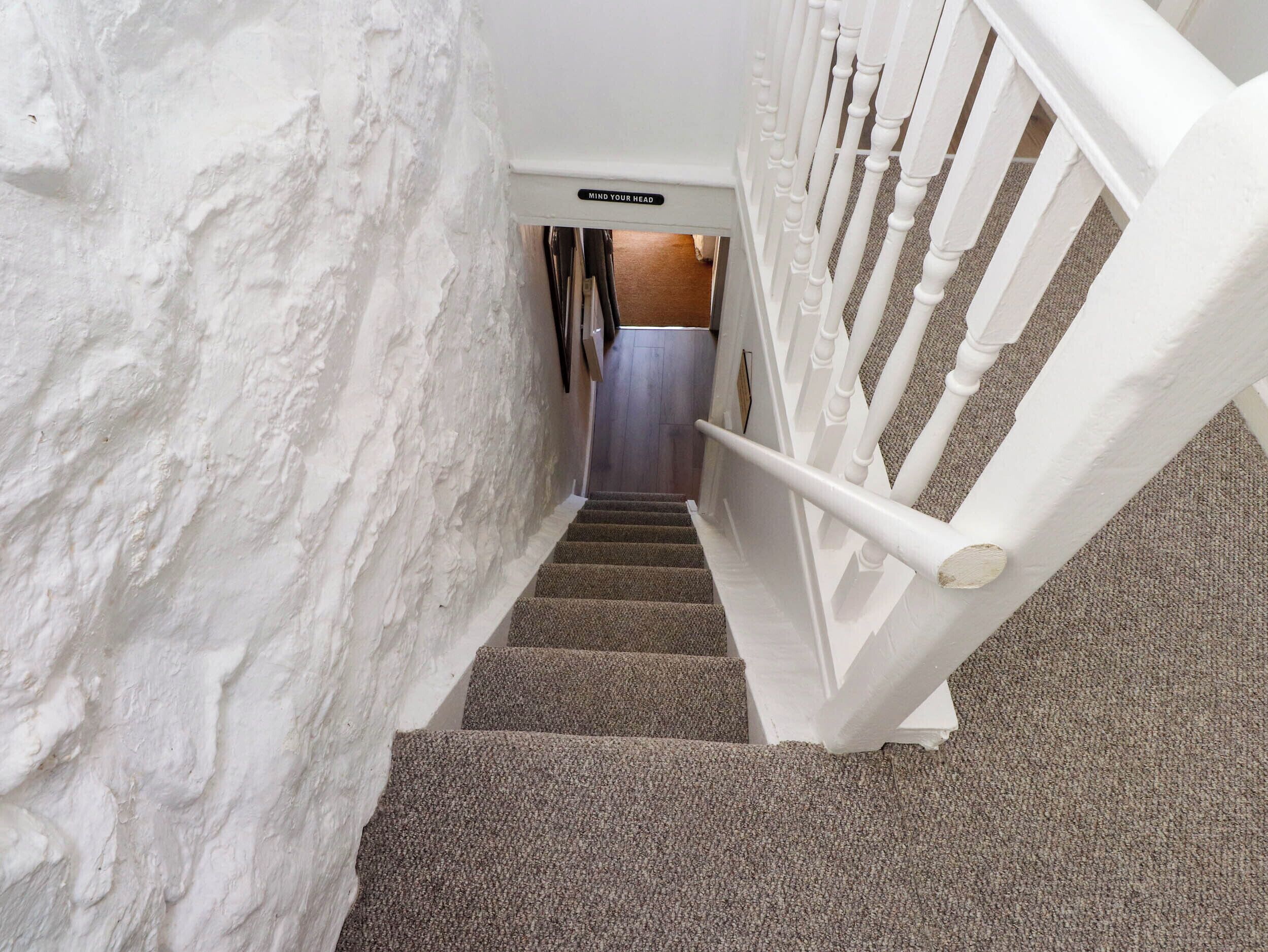 Una escalera con paredes blancas y suelo alfombrado que conduce a una habitación con una puerta.