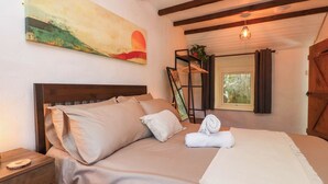 A bedroom with a wooden bed, a bedside table, a nightstand, a painting, a window with curtains, and a hanging light fixture.
