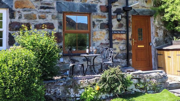 A stone building with a wooden door, a window, and a small outdoor seating area with two chairs and a table.