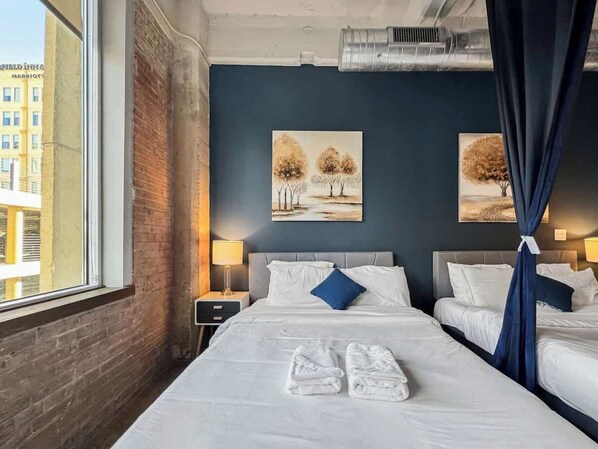 A hotel room with two beds, a view of a building outside, and artwork on the wall.