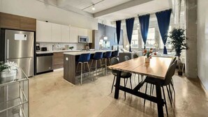 A modern kitchen with stainless steel appliances, a central island with bar stools, and a dining table.