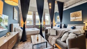 A modern hotel room with a large bed, a sofa, a desk, and a view of the city.