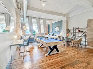 Una habitación amplia con mesa de billar, un conjunto de sofás y una estantería.