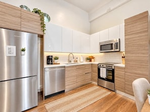 A modern kitchen with stainless steel appliances, white cabinetry, and a wooden floor. - Stylish 2BR | Heart of Town | Host 16 | Valet Park (Dallas)