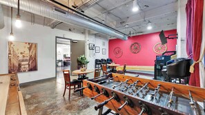 A room with a foosball table, a red wall with decorative wheels, and a jukebox. - Elegant 2BD | DT Dallas | Sleeps 16 | ValetParking (Dallas)