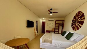 Ein Zimmer mit einem Bett, einer Hängematte, einem Tisch, einem Fernseher und einem Deckenventilator.