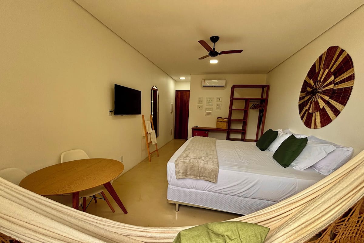 A room with a bed, a hammock, a table, a TV, and a ceiling fan.