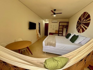 Ein Zimmer mit einem Bett, einer Hängematte, einem Tisch, einem Fernseher und einem Deckenventilator.
