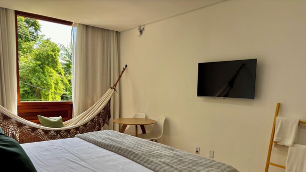 Ein Hotelzimmer mit Bett, Hängematte, Fernseher, Stuhl und einer Holzleiter.