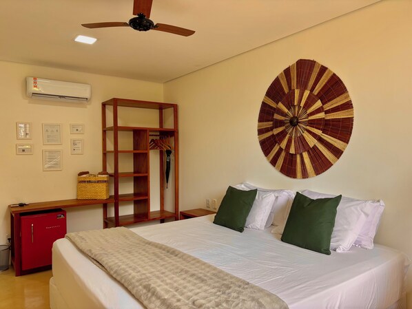 A hotel room with a bed, a ceiling fan, an air conditioning unit, a wall-mounted decorative fan, a wooden shelf with a basket, and a red safe. - Pousada Mel do Cacau (Itacare)