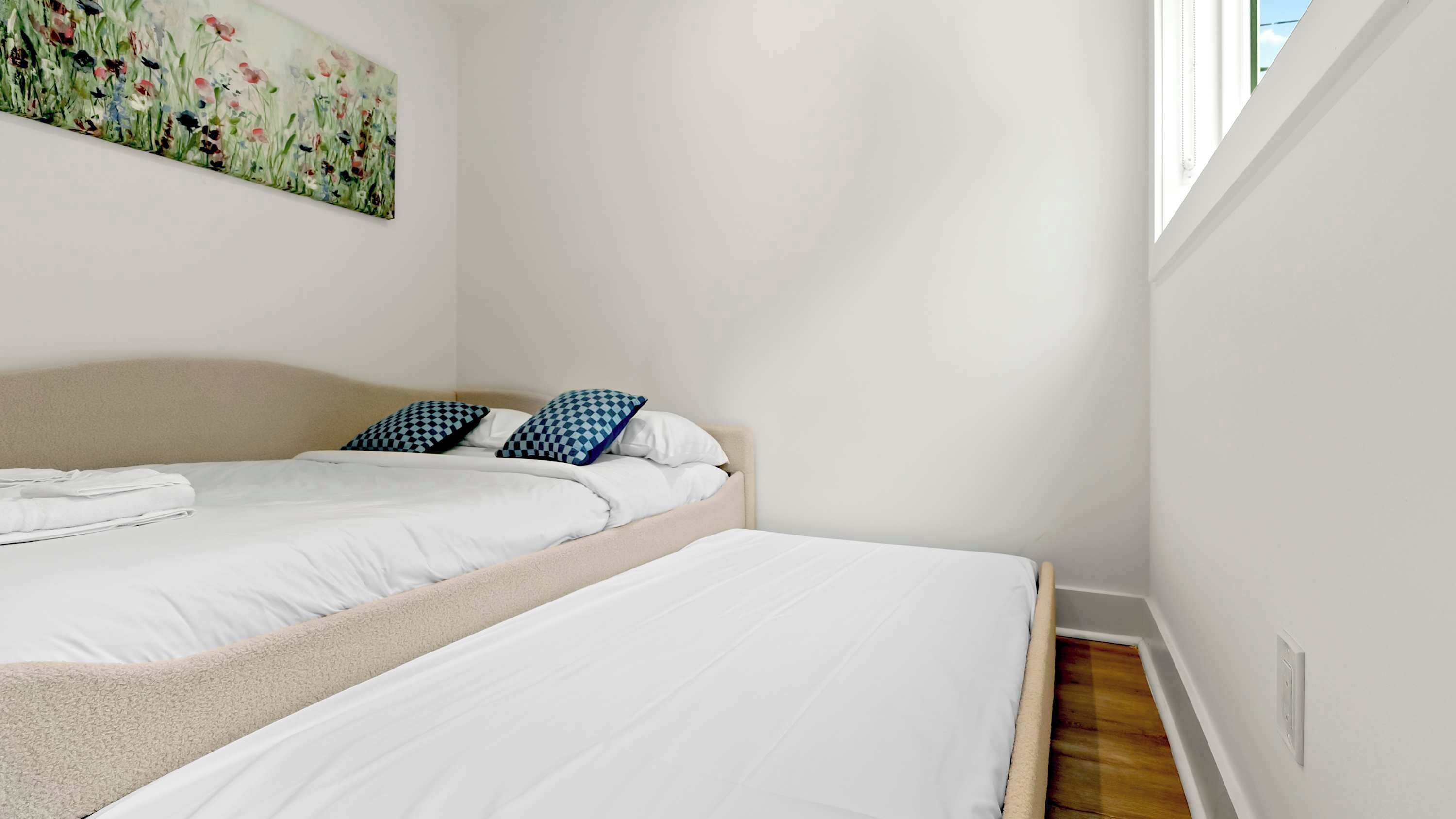 A bedroom with two beds, a window, and a painting on the wall.