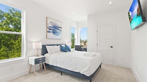 A bedroom with a bed, bedside tables, a TV, and large windows.