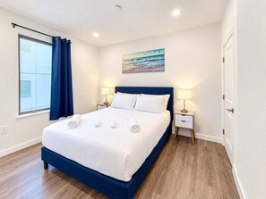 A hotel room with a large bed, two bedside tables with lamps, a painting on the wall, and a window with curtains.
