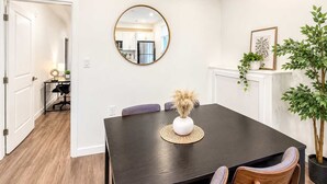 Een eetgedeelte met een donker houten tafel, twee stoelen, een ronde spiegel en een potplant.