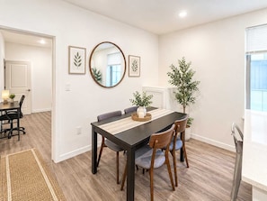 A dining area with a dark wooden table, light-colored chairs, and a mirror above.