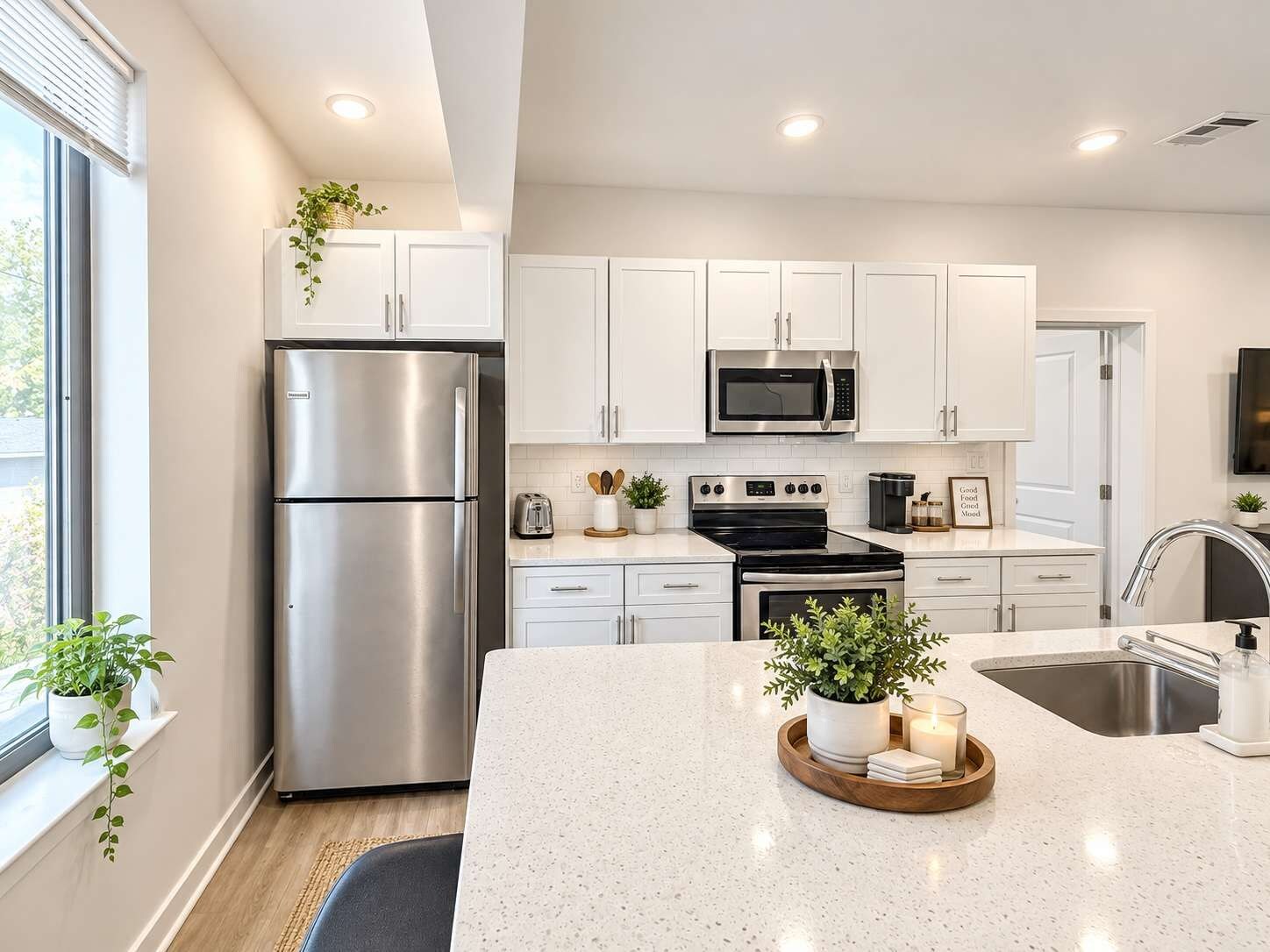 Una cocina moderna con armarios blancos, electrodomésticos de acero inoxidable y una isla central con plantas.