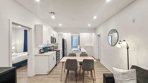 A modern kitchen with white cabinets, a dining table with chairs, a black sofa with a pillow, and a floor lamp. - Ideal 2BD Retreat | Sleeps 6 | Center City Philly (Philadelphia)