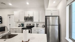 A modern kitchen with white cabinets, stainless steel appliances, and a large window.