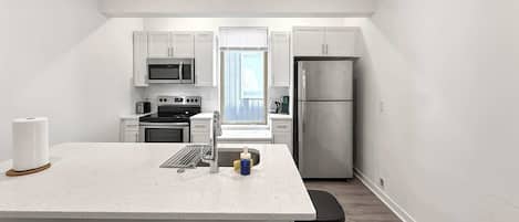 A modern kitchen with white cabinetry, stainless steel appliances, and a central island with seating.