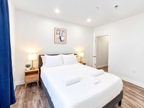 A hotel room with a bed, two bedside tables with lamps, a door, and a wall-mounted painting.