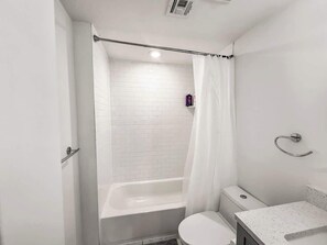 A small, modern bathroom with a white bathtub, a toilet, and a sink.