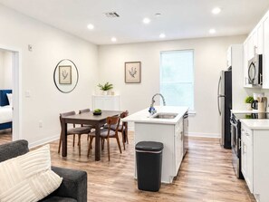 A modern kitchen with a dining area, white cabinetry, and a window with blinds. - Inviting 2BD | Sleeps 6 | Northern Liberties (Philadelphia)