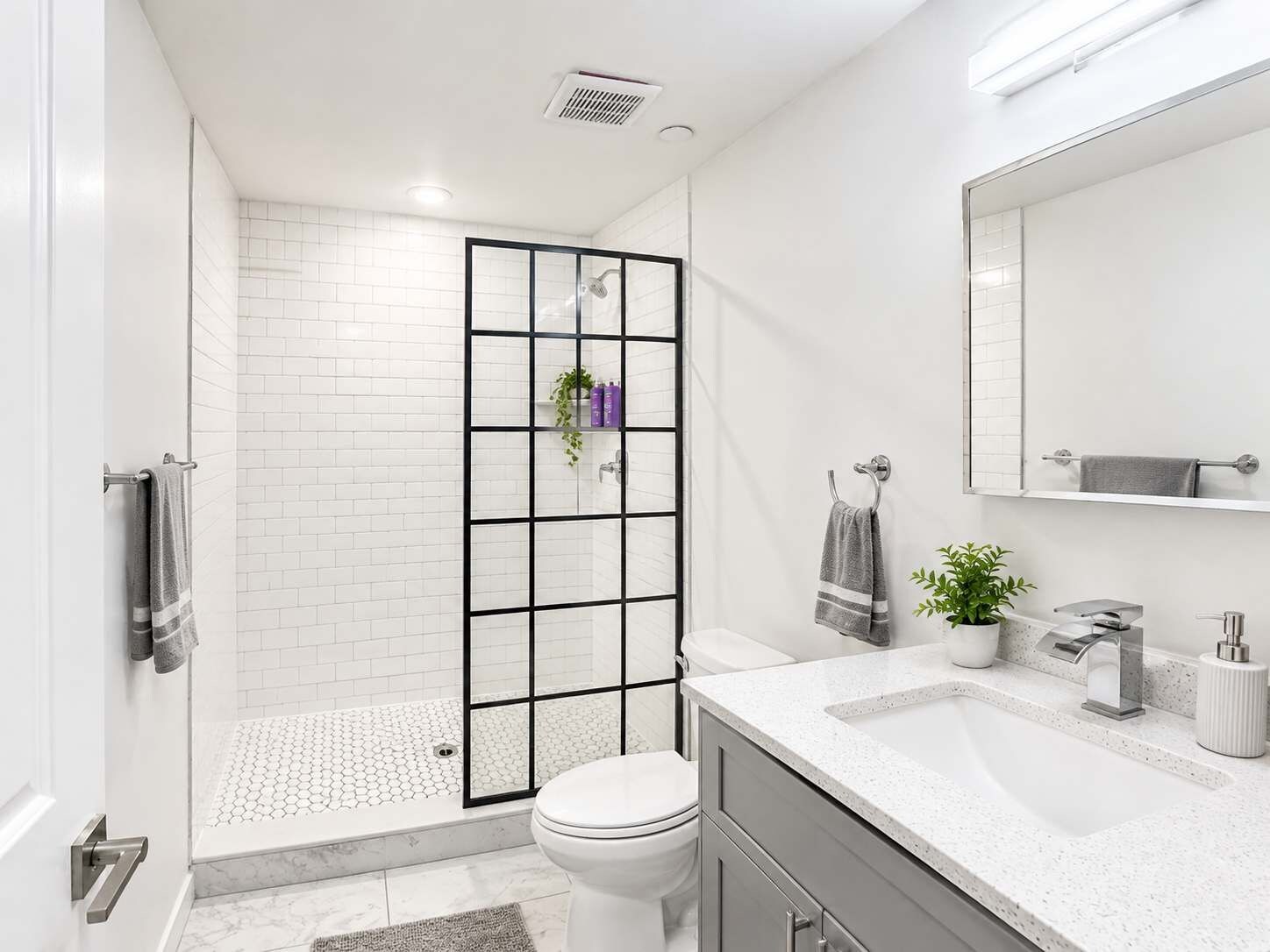 Un baño moderno con cabina de ducha de vidrio, inodoro blanco, lavamanos con espejo y una planta en maceta.