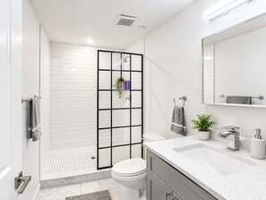 A modern bathroom with a glass shower enclosure, a white toilet, a sink with a mirror, and a potted plant. - Inviting 2BD | Sleeps 6 | Northern Liberties (Philadelphia)