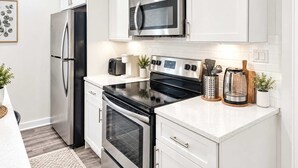 A modern kitchen with stainless steel appliances, white cabinetry, and a countertop with a coffee maker and utensils. - Inviting 2BD | Sleeps 6 | Northern Liberties (Philadelphia)