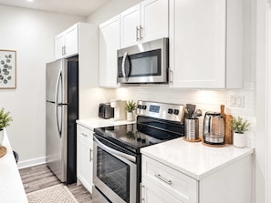 Cocina moderna con electrodomésticos de acero inoxidable, muebles blancos y una encimera con cafetera y utensilios.